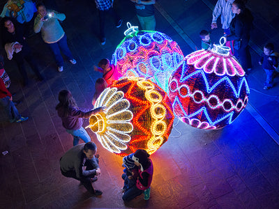 Giant pre-lit LED ornaments displayed outdoors at night, glowing with multiple colors.